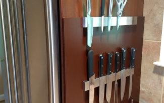 Knives and a pair of scissors on magnetic knife bars attached to a wooden mount.